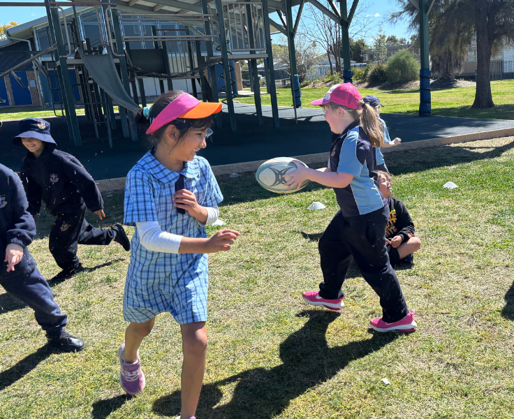 photo of students playing with a football on the grass area near the play equopment