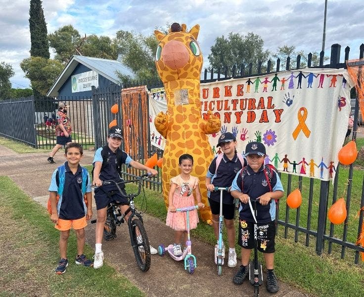 photo of 5 students with scooters and bikes with a staff member dressed in a giraffe costume